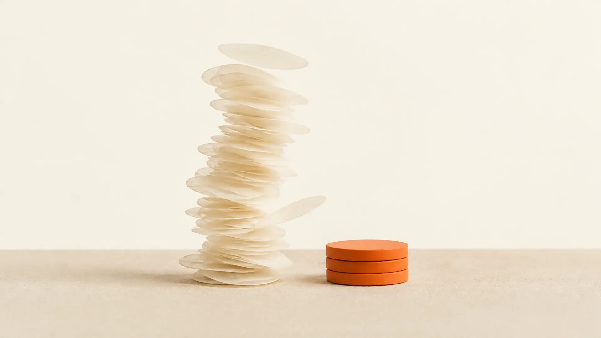 A tall wobbling stack of pale paper discs beside a short, solid stack of orange discs