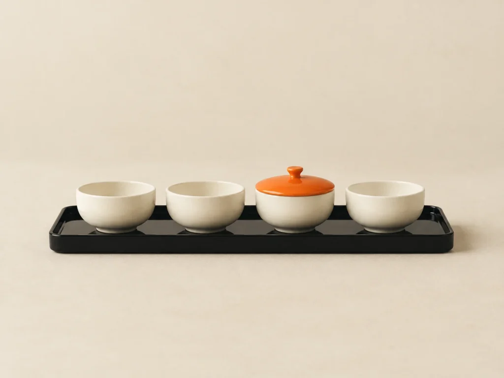 Four cream cups on a black tray, one of them closed with an orange lid